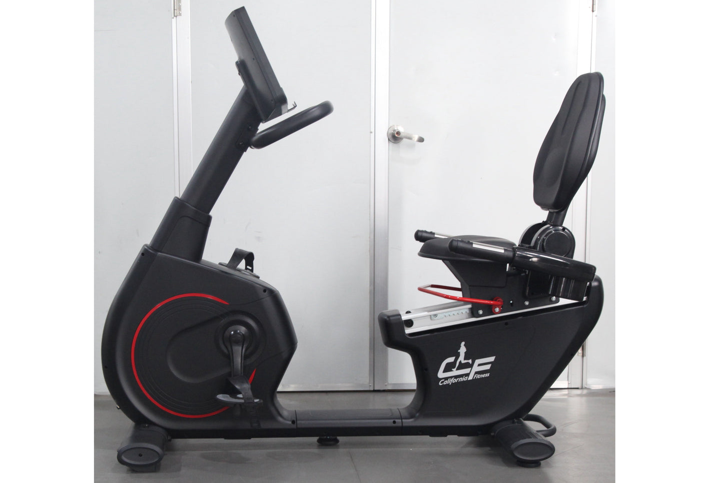 California Fitness RB8 recumbent exercise bike with black frame, red accent wheel, padded seat and backrest, displayed on gra