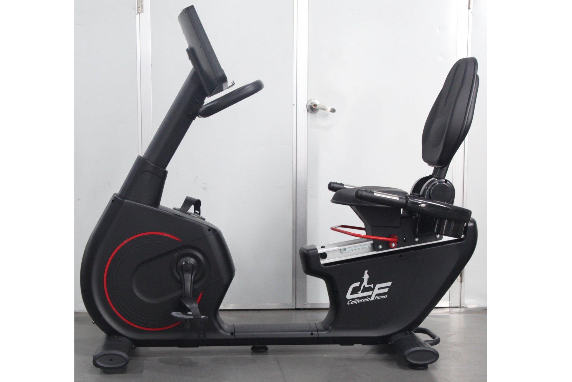 California Fitness RB8 recumbent exercise bike with black frame, red accent wheel, padded seat and backrest, displayed on gra