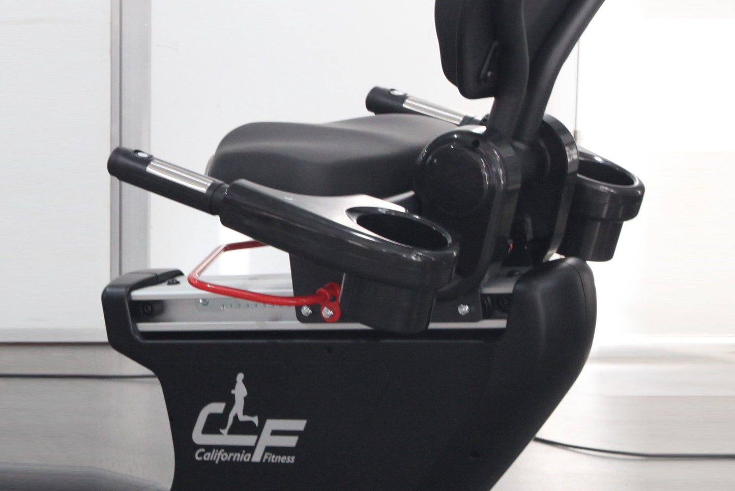 Black California Fitness recumbent exercise bike with padded seat, red foot pedal straps, and chrome-accented handles on whit