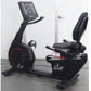 Black recumbent exercise bike with red accents, digital display console, padded seat, and footrest on gray background