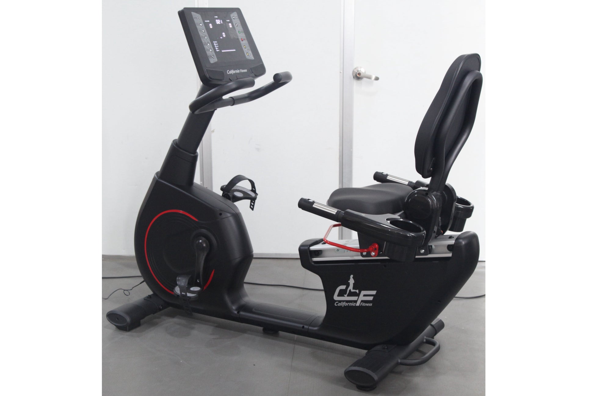 Black recumbent exercise bike with red accents, digital display console, padded seat, and footrest on gray background