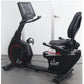 Black recumbent exercise bike with digital console, red wheel accent, and padded seat on gray background
