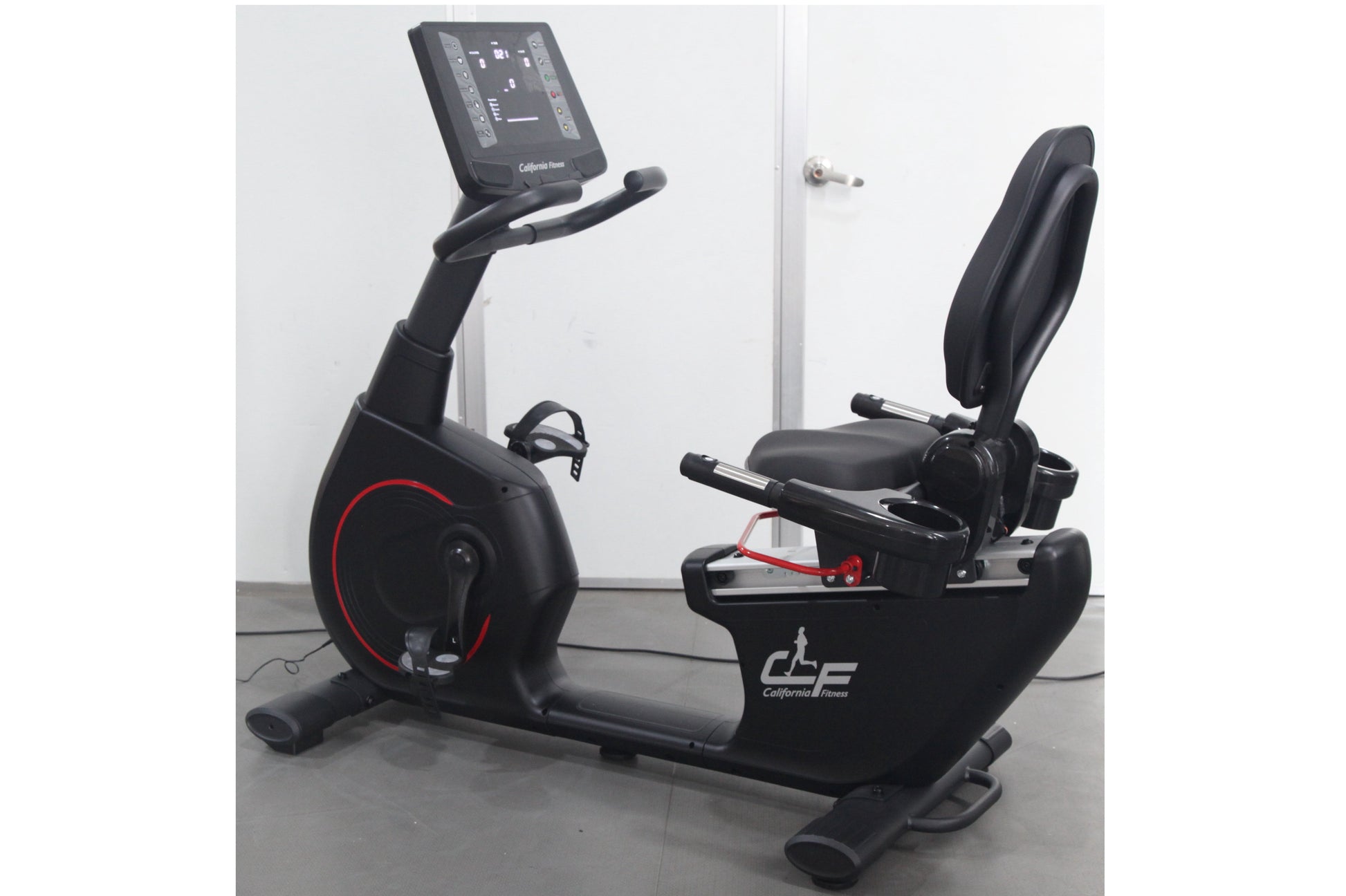 Black recumbent exercise bike with digital console, red wheel accent, and padded seat on gray background