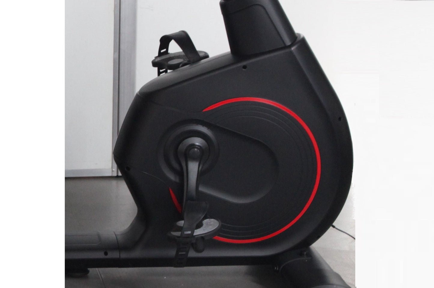 Black recumbent exercise bike with red circular accent design and digital display, side view on white background