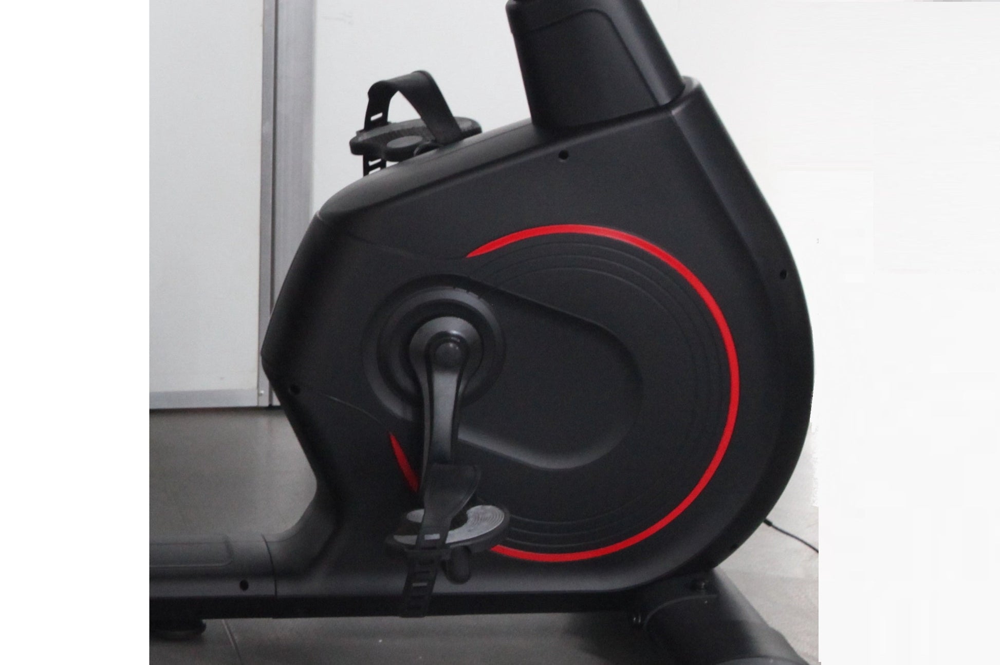 Black recumbent exercise bike with red circular accent design and digital display, side view on white background