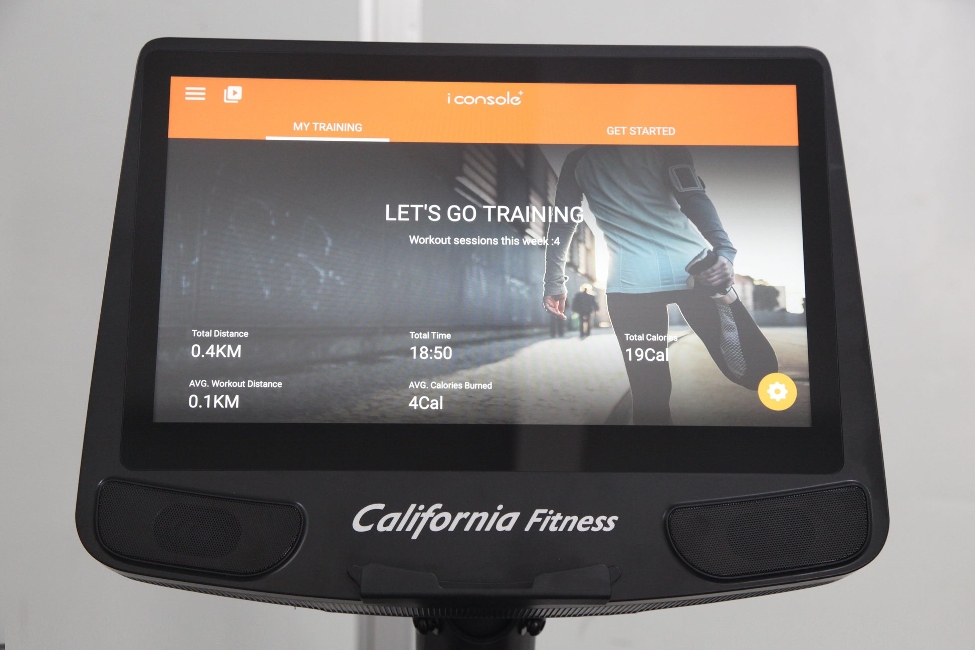 Black recumbent exercise bike with integrated touchscreen display showing iConsole training app interface, orange navigation 