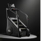 Black and silver commercial stair climber with digital display console, handrails, and stepped platform on dark background