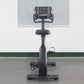 Black upright exercise bike with digital display console, padded seat, handlebars, and pedals on stable base, front view