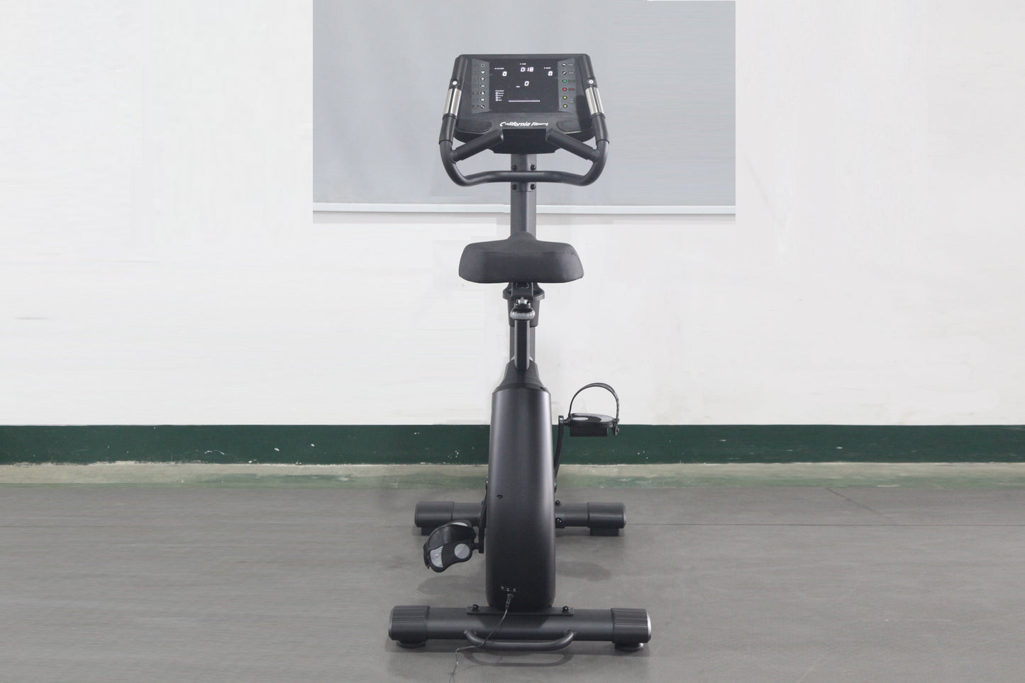 Black upright exercise bike with digital display console, padded seat, handlebars, and pedals on stable base, front view