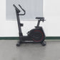 California Fitness U8 upright exercise bike with black frame, red wheel accents, padded seat, and handlebars on gray floor
