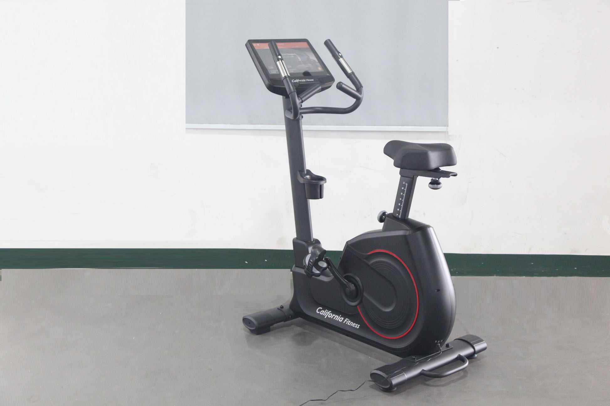 Black upright exercise bike with red accents, digital display console, and black padded seat on gray floor