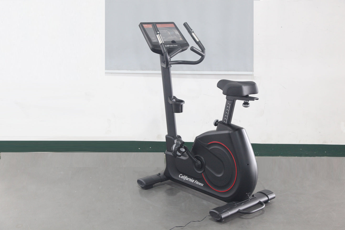 Black upright exercise bike with red accents, digital display console, and black padded seat on gray floor