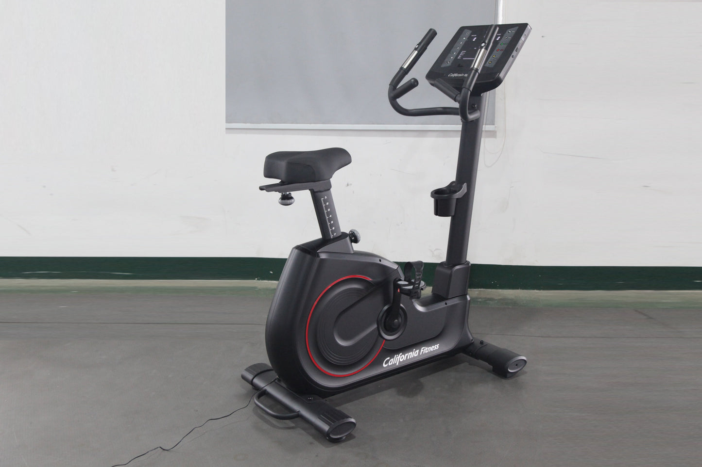 California Fitness U8 black upright exercise bike with red accents, digital display console, and padded seat on gray floor