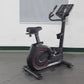 California Fitness U8 black upright exercise bike with red accents, digital display console, and padded seat on gray floor