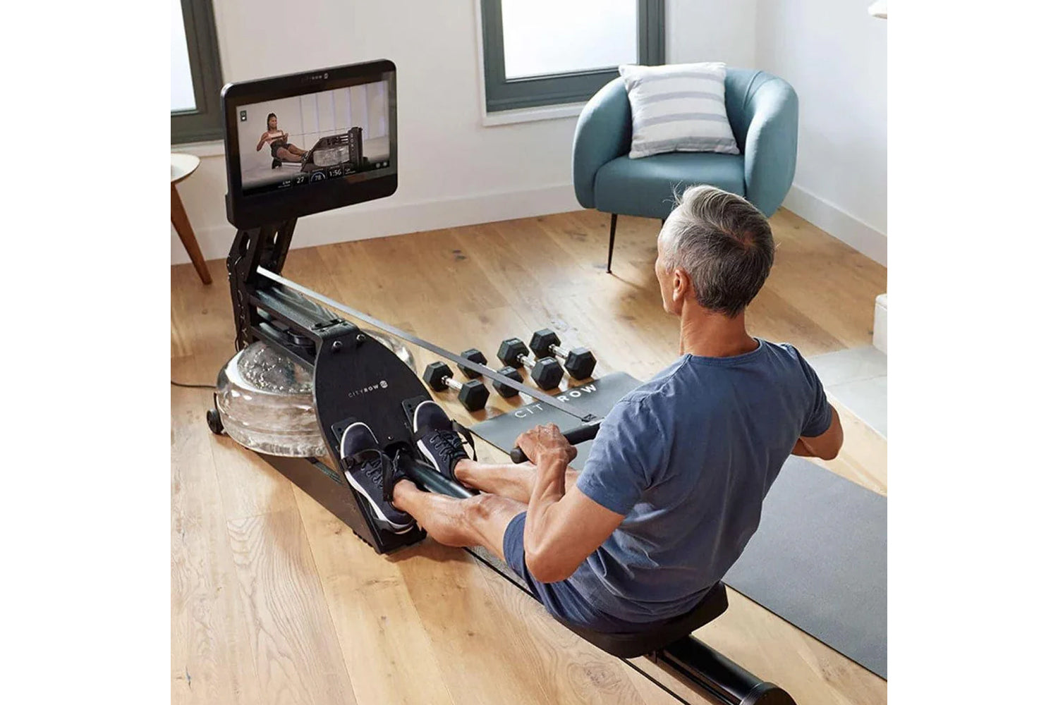 Black and wood water rowing machine with digital display, dumbbell storage, and footplate, used by man in home gym setting