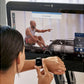 Person wearing smartwatch viewing CityRow GC rowing machine display screen showing instructor-led workout with performance me