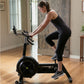 Woman wearing black tank top and capri leggings riding Concept2 BikeErg stationary bike in home gym setting