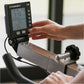 Concept2 PM5 black digital monitor displaying workout metrics, held by model's hand above stationary bike equipment
