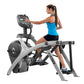 Woman in blue tank top using Cybex 525AT Total Body Arc Trainer elliptical with digital console on white background