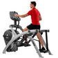 Man in red shirt and black shorts using stationary arc trainer with digital console on white background