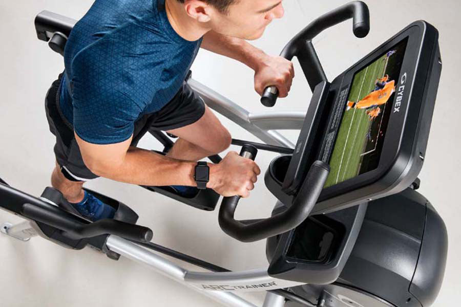 Man in blue shirt using black and silver elliptical trainer with digital display screen showing workout metrics