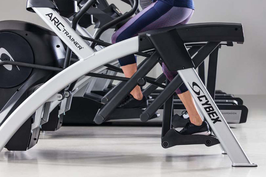 Person in purple leggings on white and black Cybex R Series Arc Trainer with digital display and foot pedals, side view