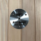 Brushed metal circular control plate labeled "MP3 AUX INPUT MAX:175mV" mounted on light wood sauna interior