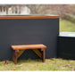 Dark grey cold plunge tub with copper trim and white interior, paired with wooden bench and black filtration unit on grass