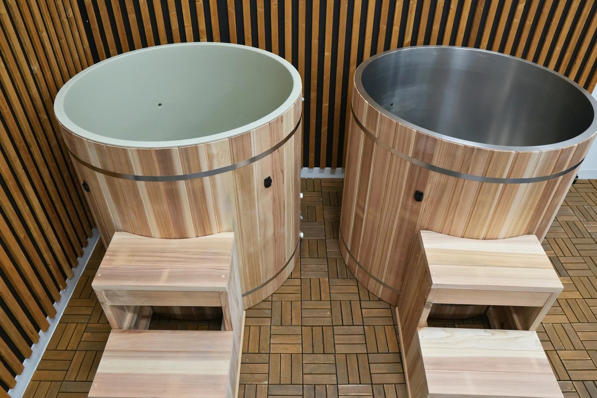 Two cedar wood barrel cold plunge tubs with light green and dark gray interiors, metal bands, and wooden step platforms on wo