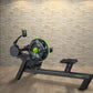 Black rowing machine with lime green accents and digital display, shown on wooden floor against cream brick wall