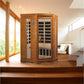 Golden wood two-person infrared sauna with glass front panels and black interior, shown in bright home interior space