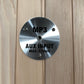 Brushed metal circular control panel with MP3 and AUX INPUT MAX 175mV text, mounted on light wood sauna wall
