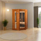 Cedar two-person infrared sauna with glass doors and interior benches, displayed in modern bedroom setting