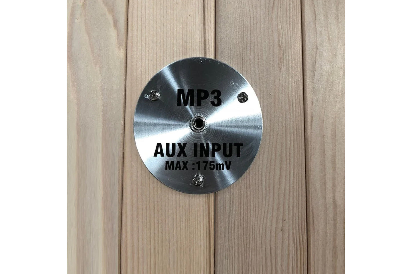 Brushed metal circular plate with MP3 and AUX INPUT MAX 175mV text mounted on light wood sauna interior