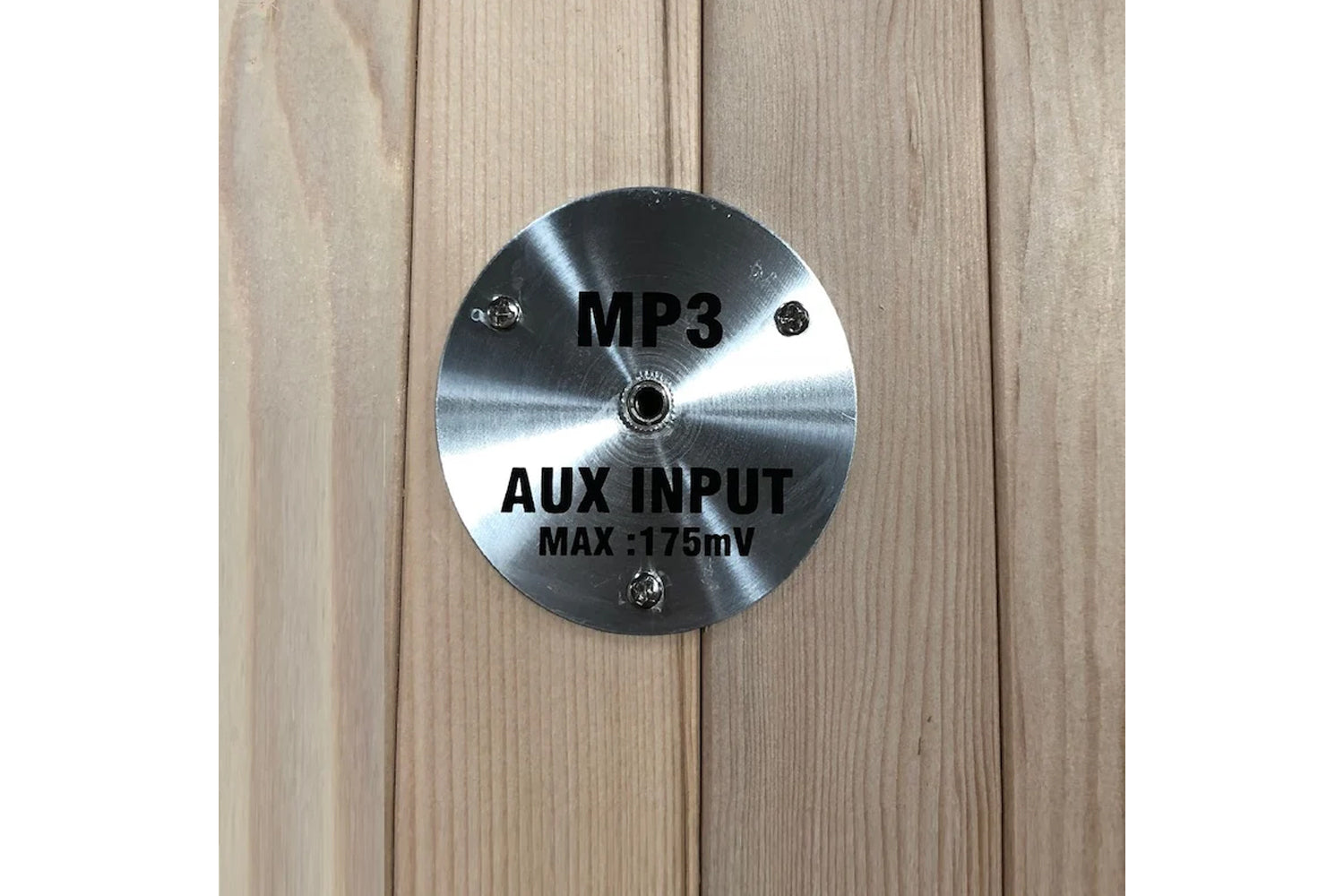Brushed metal circular plate with MP3 and AUX INPUT MAX 175mV text mounted on light wood sauna interior