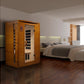 Two-person infrared sauna with golden-brown wood exterior and glass door, displayed in modern bedroom setting