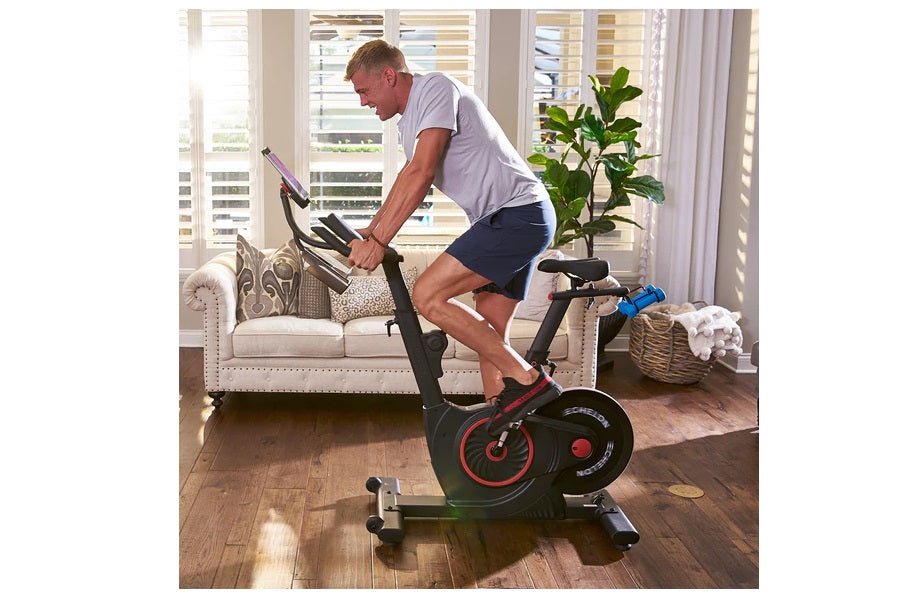 Man exercising on black and red stationary bike in living room with white sofa in background