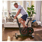 Man exercising on black and red stationary bike in living room with white sofa in background