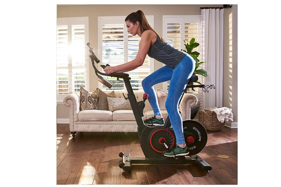 Woman on stationary exercise bike with black frame and red accents in home living room setting