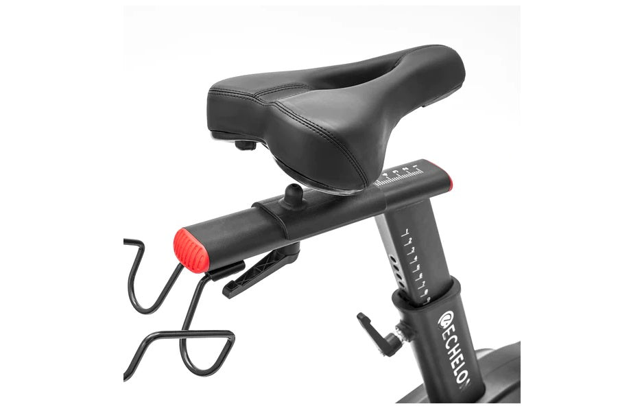 Black stationary exercise bike with padded seat, digital display console, and red rear tail light on white background