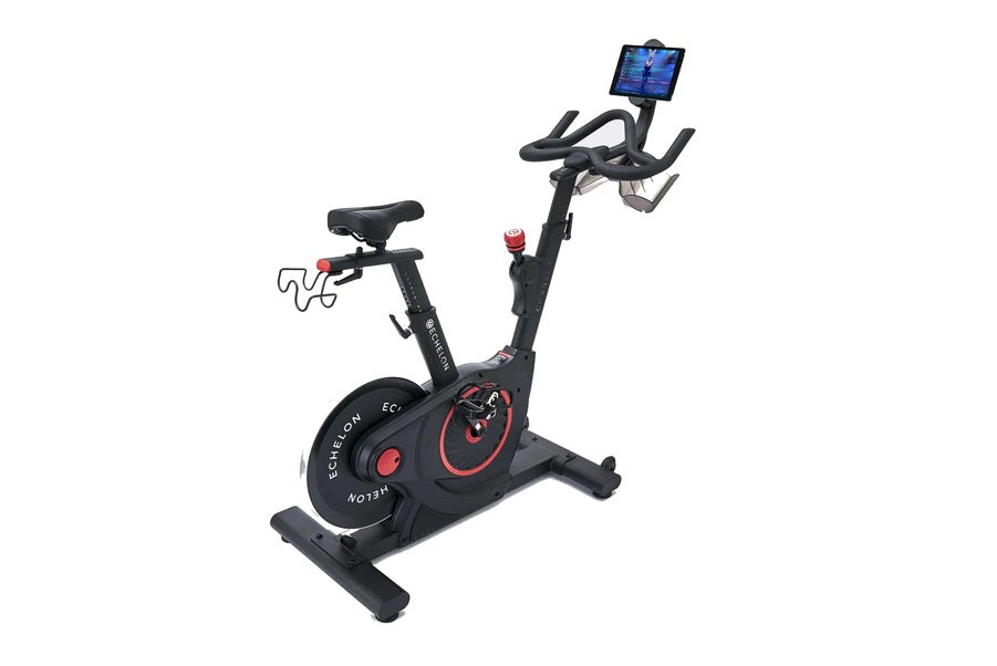 Black and red upright stationary exercise bike with tablet holder, handlebar grips, and weighted flywheel on white background