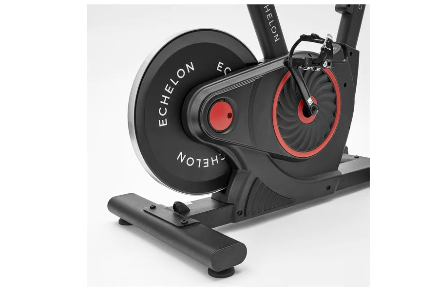 Black and red stationary exercise bike with large flywheel, pedals, and handlebars on white background
