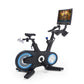 Black stationary exercise bike with blue accent wheels and handlebar monitor displaying workout video on white background