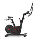 Black and red stationary indoor exercise bike with digital display and adjustable handlebars on white background