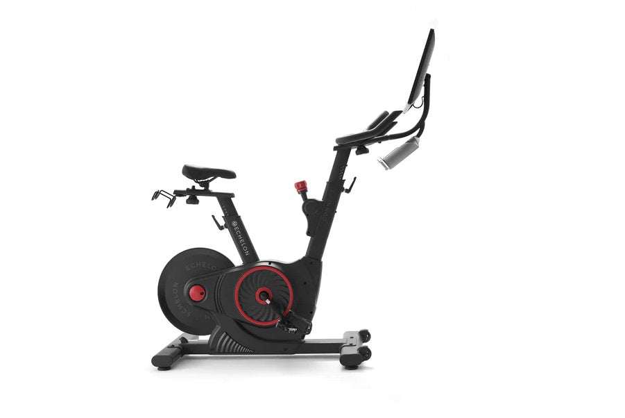 Black and red stationary indoor exercise bike with digital display and adjustable handlebars on white background