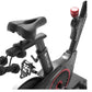 Black and red stationary exercise bike with padded seat, digital display, pedals with straps, and handlebars with red accent 