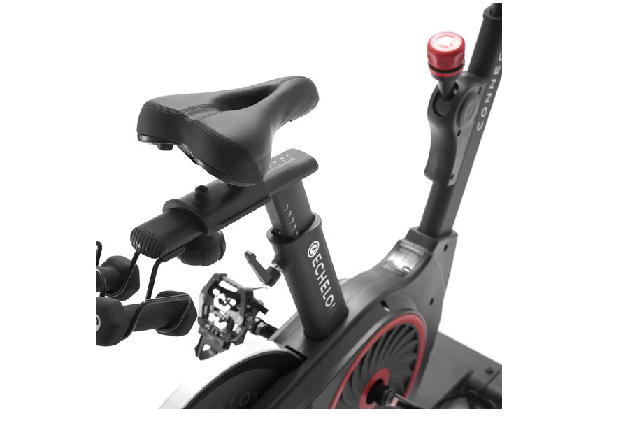 Black and red stationary exercise bike with padded seat, digital display, pedals with straps, and handlebars with red accent 