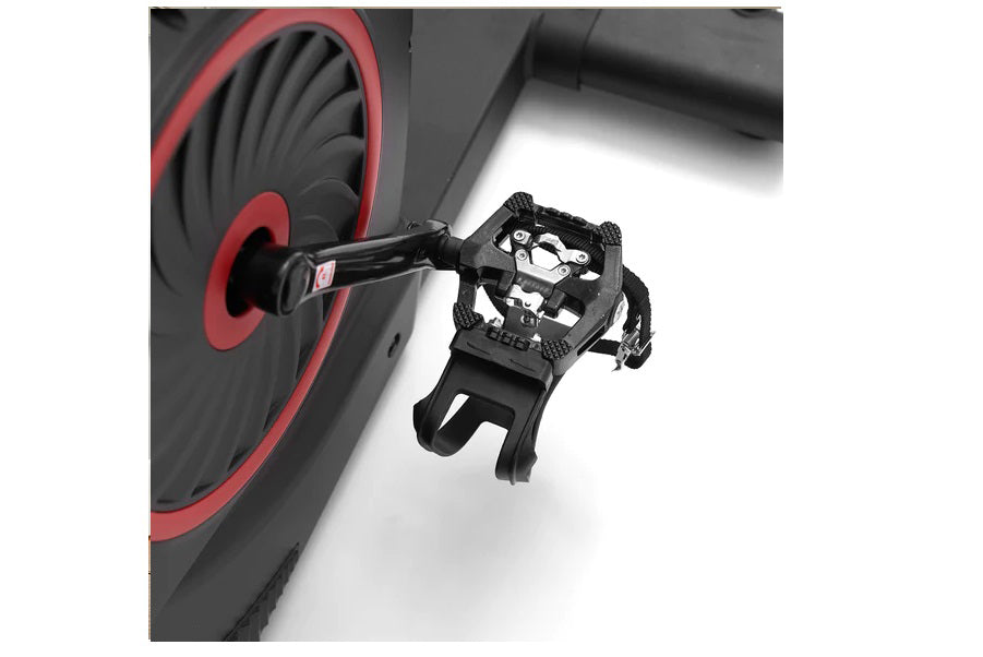 Black platform pedal with mesh straps attached to red and black exercise bike wheel, detail view