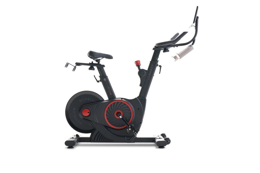 Black and red indoor stationary exercise bike with dual handlebar options and weighted flywheel on white background