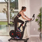 Woman in black sports bra and leggings riding black and red stationary exercise bike indoors